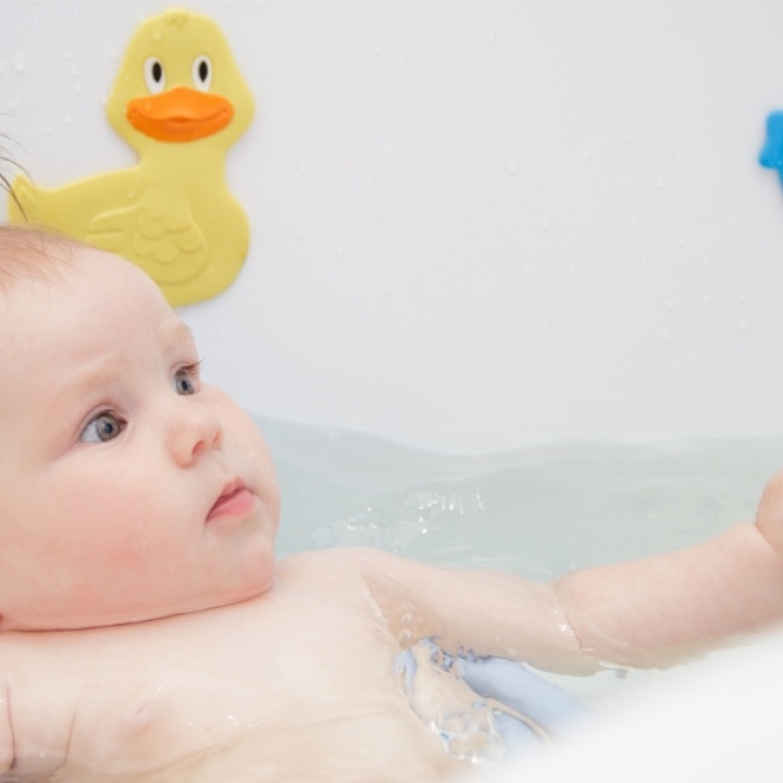 bathing a baby in a bath with a yellow rubber duck in picture
